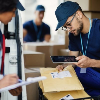 young-delivery-man-using-digital-tablet-scanning-bar-code-package-label-while-preparing-shipment-with-his-coworker-scaled.jpg